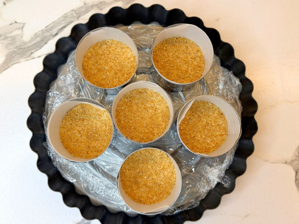 Graham cracker crust pressed into the bottoms of six mini dessert molds.