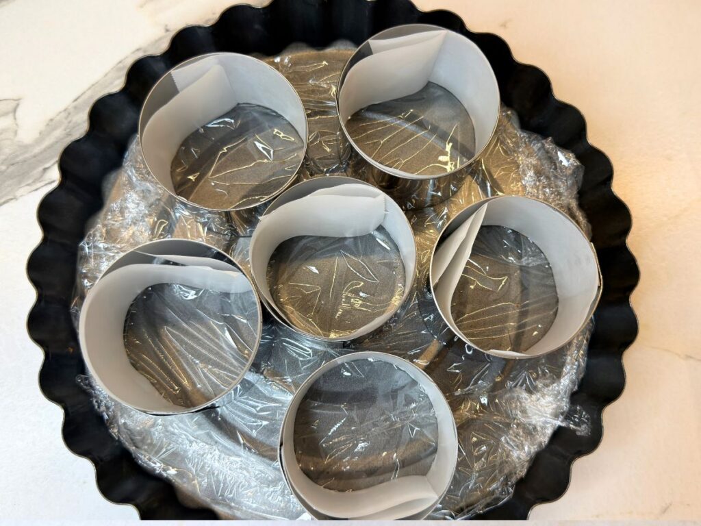 Mini dessert molds lined with parchment paper for easy cheesecake removal.