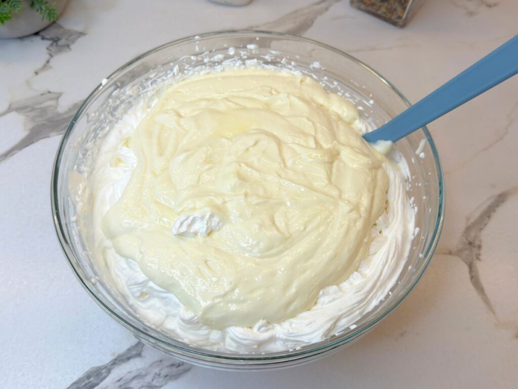 Whipped cream and cream cheese mixture combined in a glass bowl.
