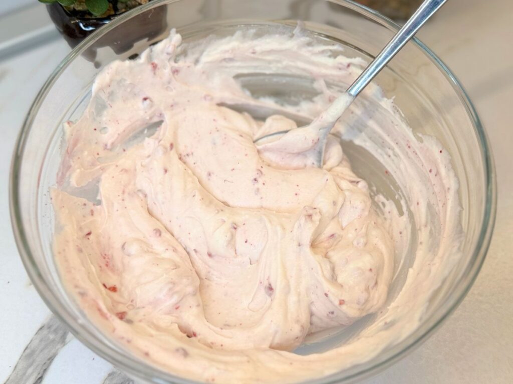 Berry topping folded into cheesecake filling to create a creamy pink layer.