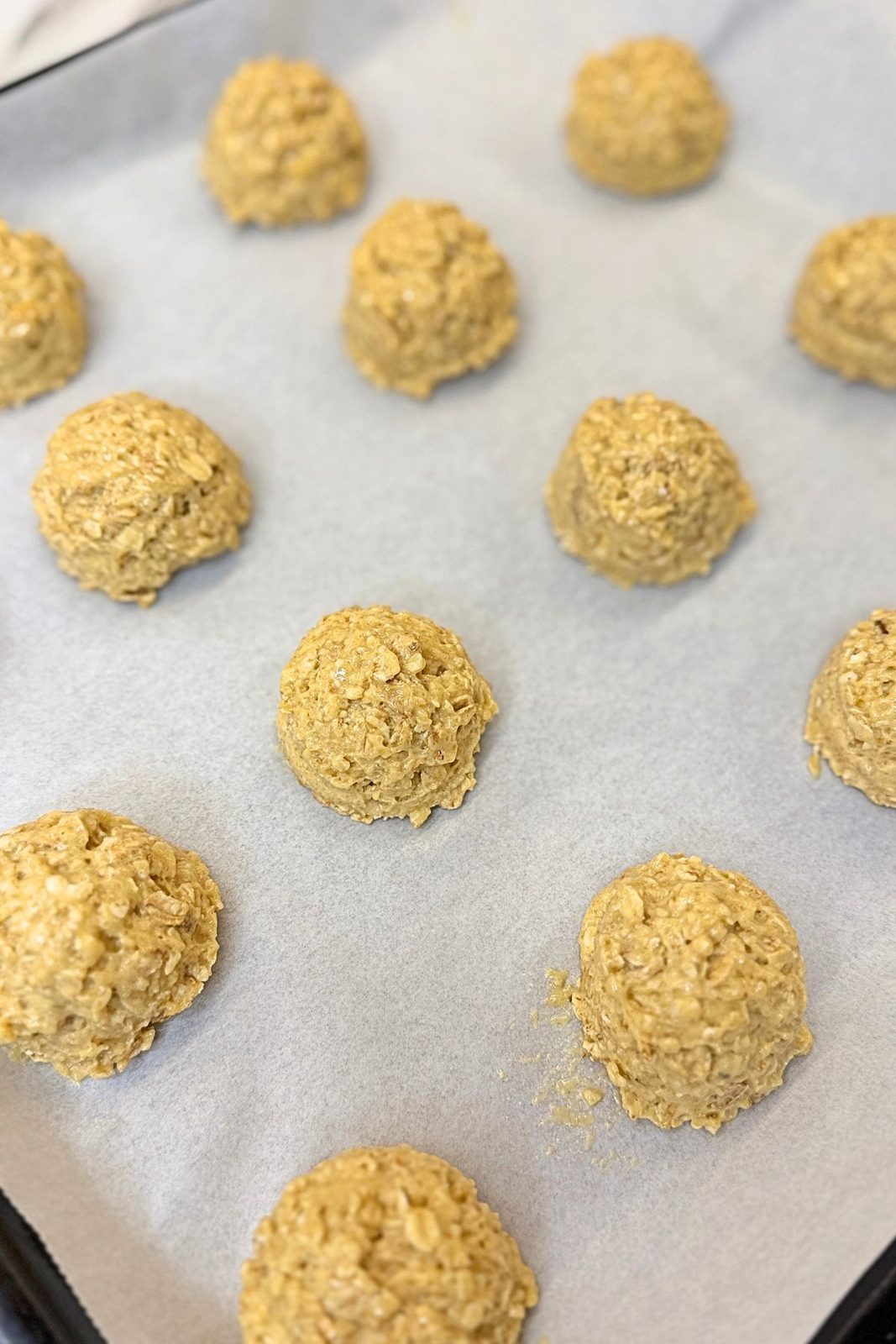 Scoops of oatmeal cookie dough arranged on a parchment-lined baking sheet