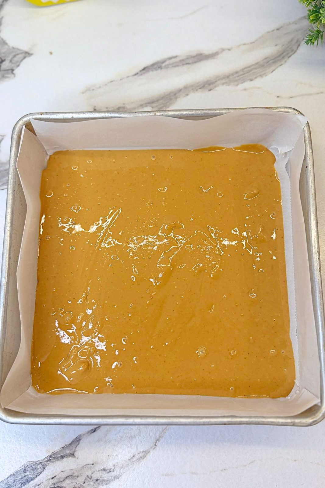 Creamy peanut butter spread evenly in a parchment-lined square baking pan before freezing.