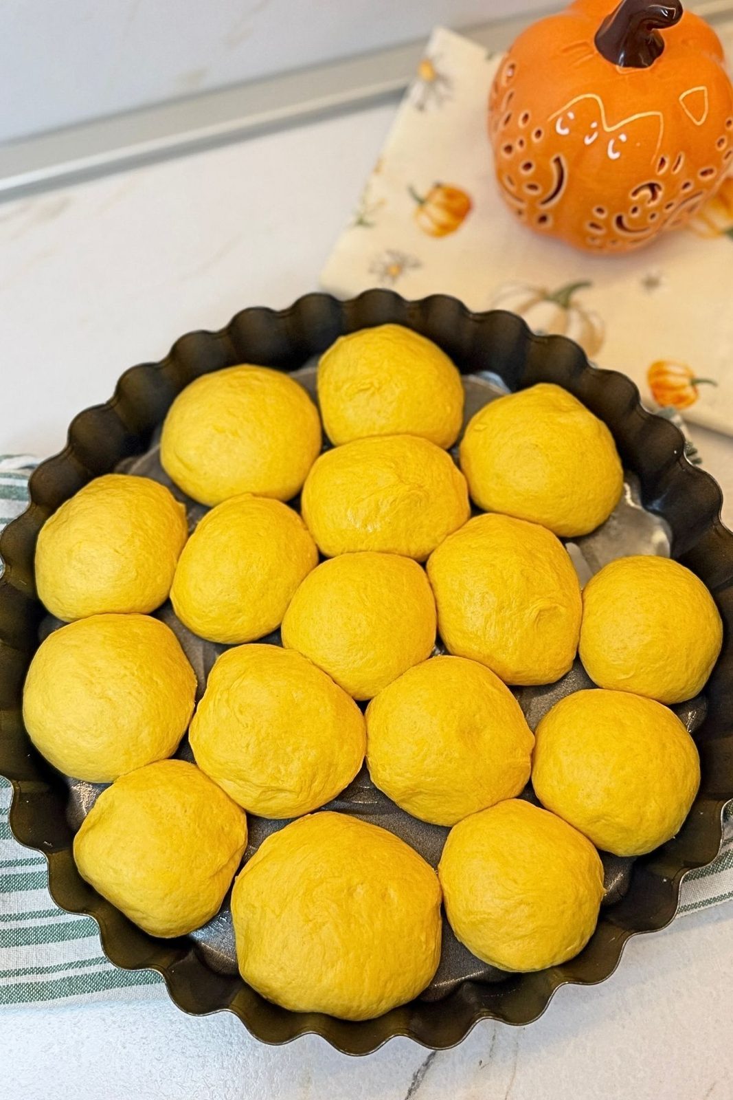 Shaped pumpkin dough balls arranged in a greased round baking pan