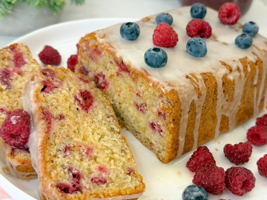 Homemade raspberry bread topped with vanilla icing and sliced to show the soft interior filled with fresh raspberries.