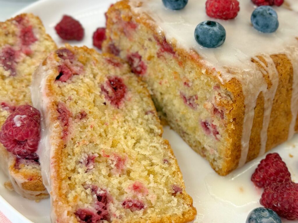 Homemade raspberry bread topped with vanilla icing and sliced to show the soft interior filled with fresh raspberries.