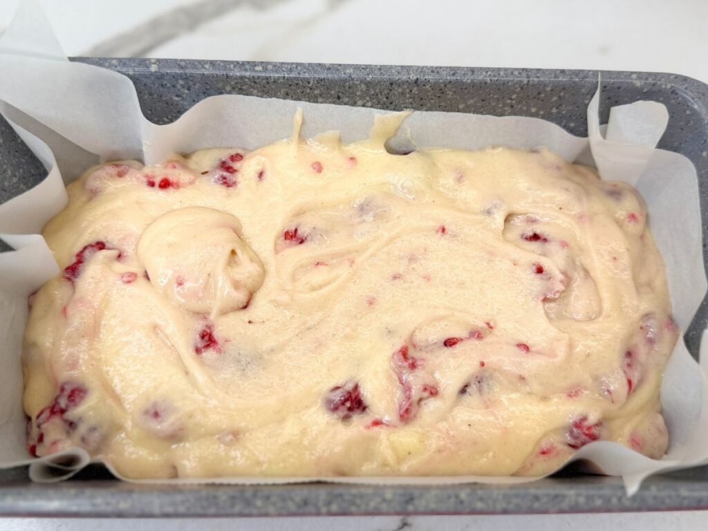 Raspberry bread batter poured into a parchment-lined loaf pan and ready for baking.