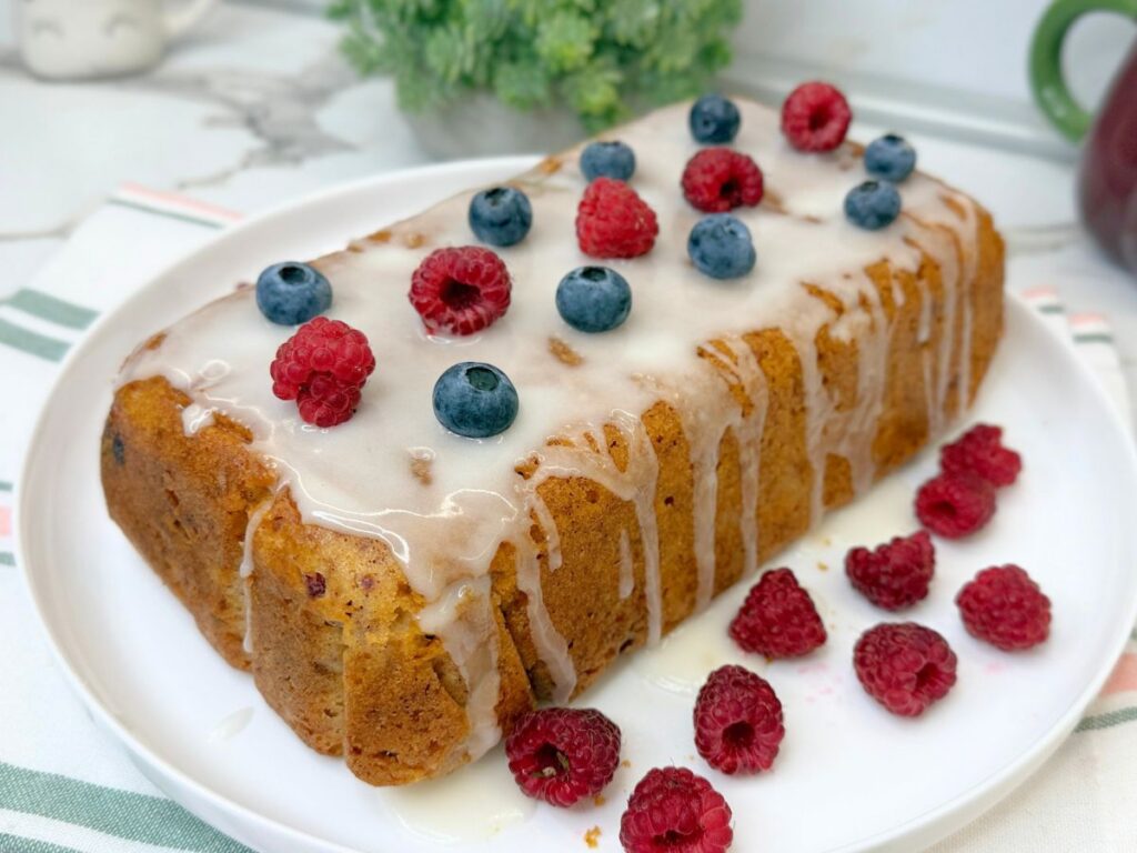 Homemade raspberry bread topped with vanilla icing and sliced to show the soft interior filled with fresh raspberries.