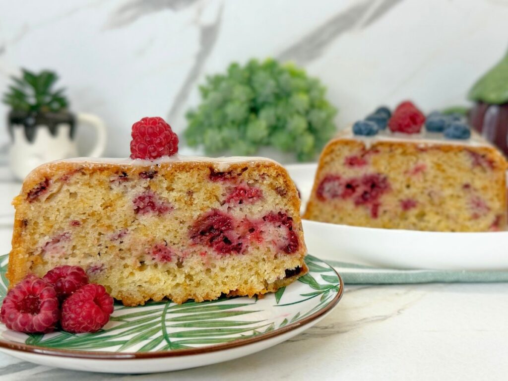 Homemade raspberry bread topped with vanilla icing and sliced to show the soft interior filled with fresh raspberries.