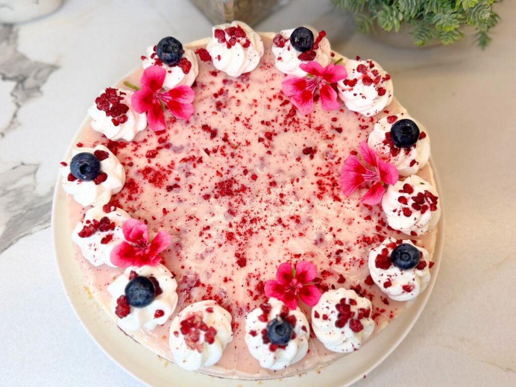 Top view of No-Bake Raspberry Cheesecake decorated with whipped cream, berries, flowers, and freeze-dried raspberries