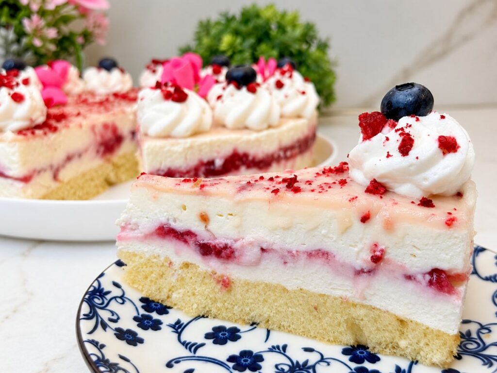 Slice of No-Bake Raspberry Cheesecake with a sponge cake base, creamy filling, raspberry layer, and white chocolate ganache