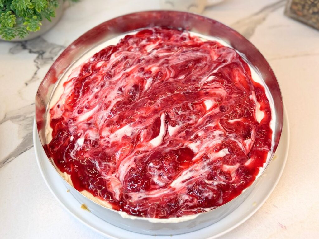 Raspberry filling spread over the creamy cheesecake layer inside a cake ring