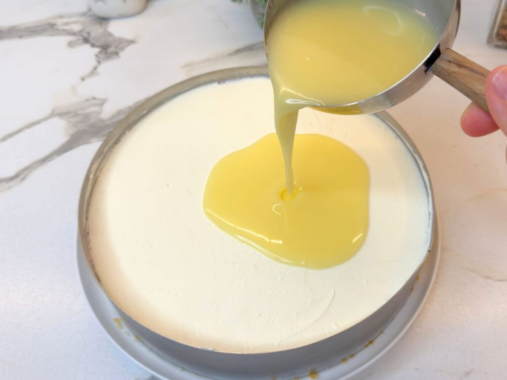 White chocolate ganache being poured over the chilled raspberry cheesecake