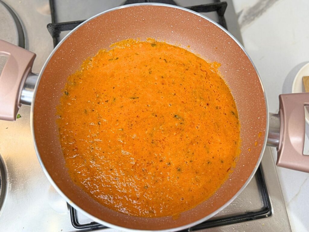 Roasted tomatoes and garlic being blended into a smooth homemade pasta sauce with an immersion blender