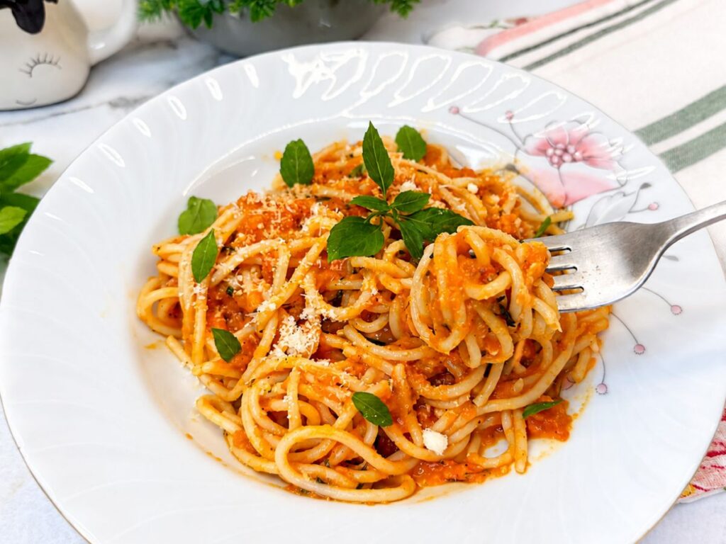 Fork lifting spaghetti coated in roasted tomato sauce with Parmesan and fresh basil