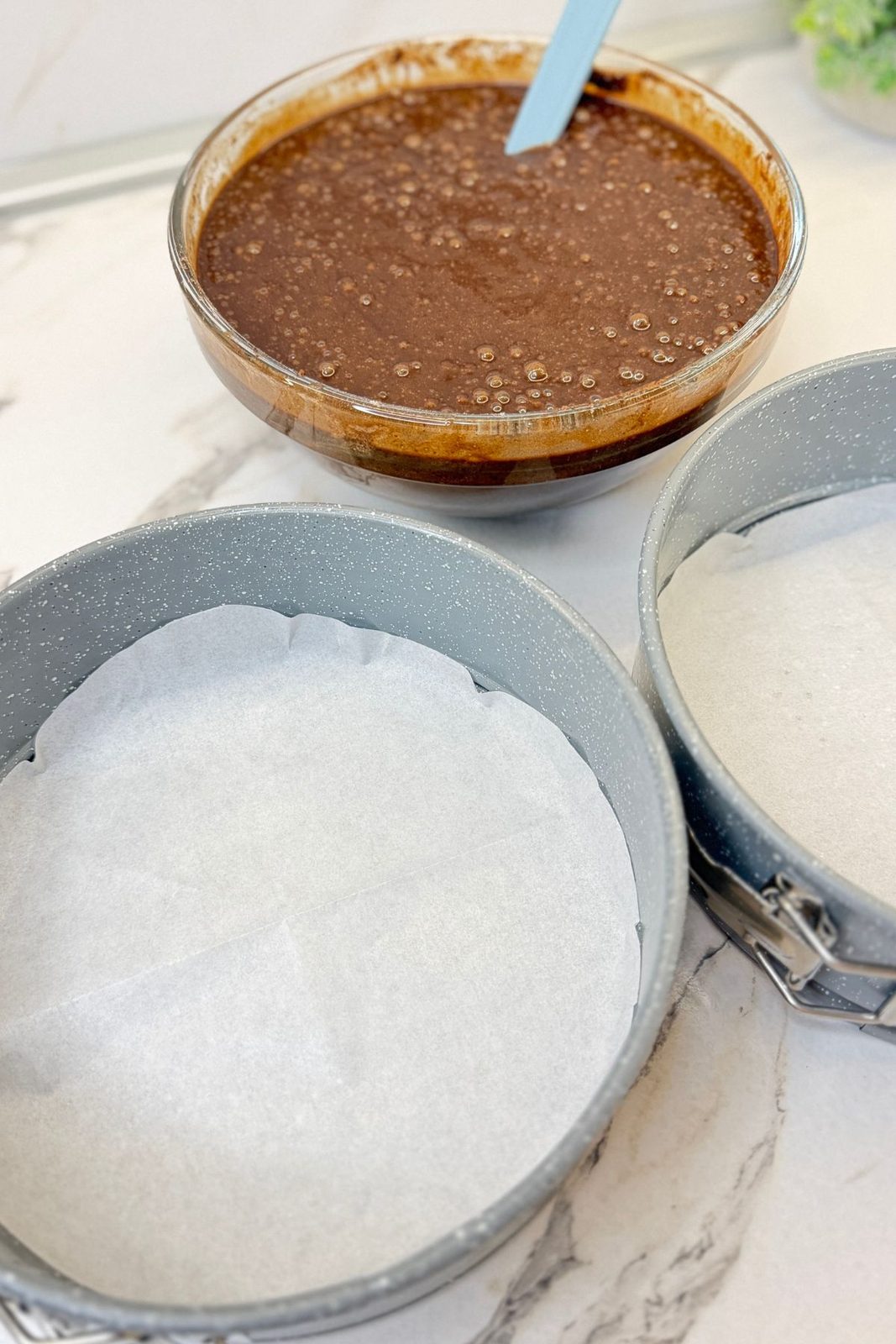 Prepared 8-inch cake pans lined with parchment beside the coffee chocolate cake batter