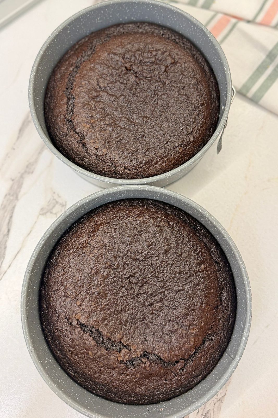 Two freshly baked coffee chocolate cake layers cooling in round cake pans