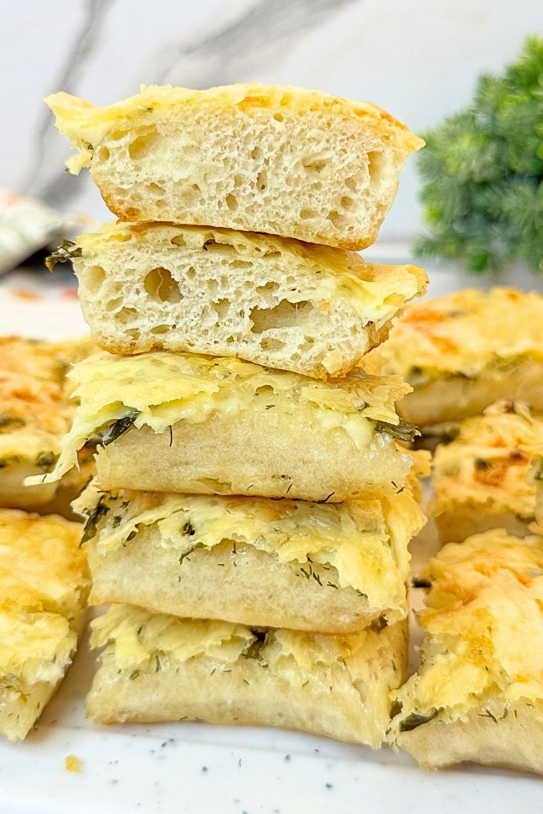 Stack of soft homemade garlic bread squares topped with melted cheese and fresh herbs