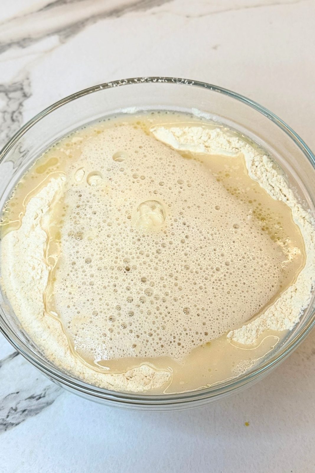 Foamy activated yeast mixture added to flour for homemade garlic bread dough
