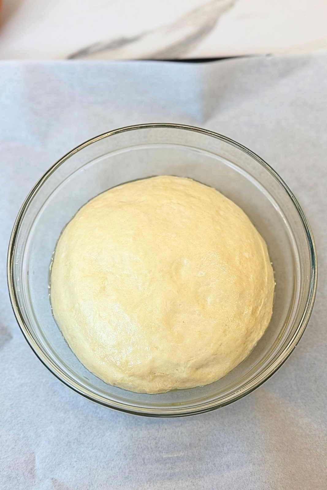 Smooth homemade garlic bread dough resting in a glass bowl
