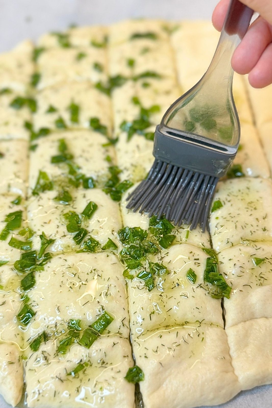 Brushing cut garlic bread dough with olive oil, garlic, and fresh herbs
