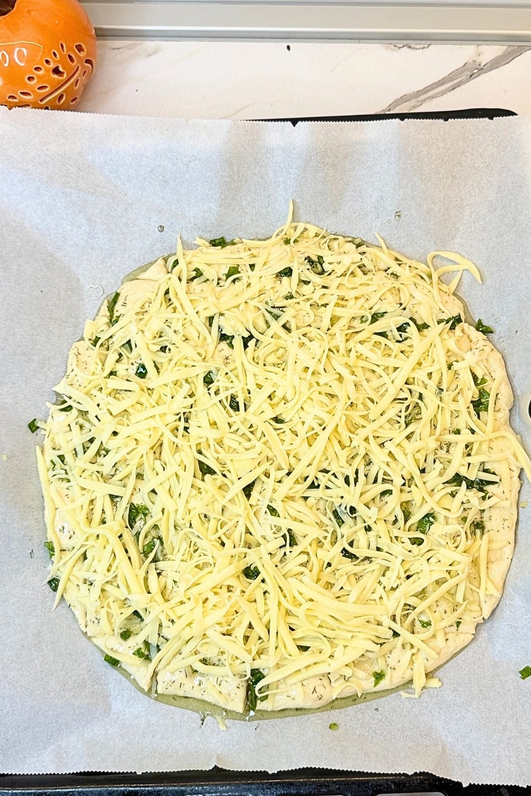 Unbaked homemade garlic bread topped with shredded cheese and fresh herbs
