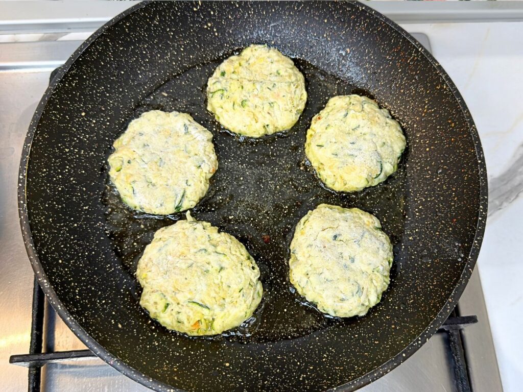 Flour-coated zucchini fritters beginning to cook in a lightly oiled skillet.
