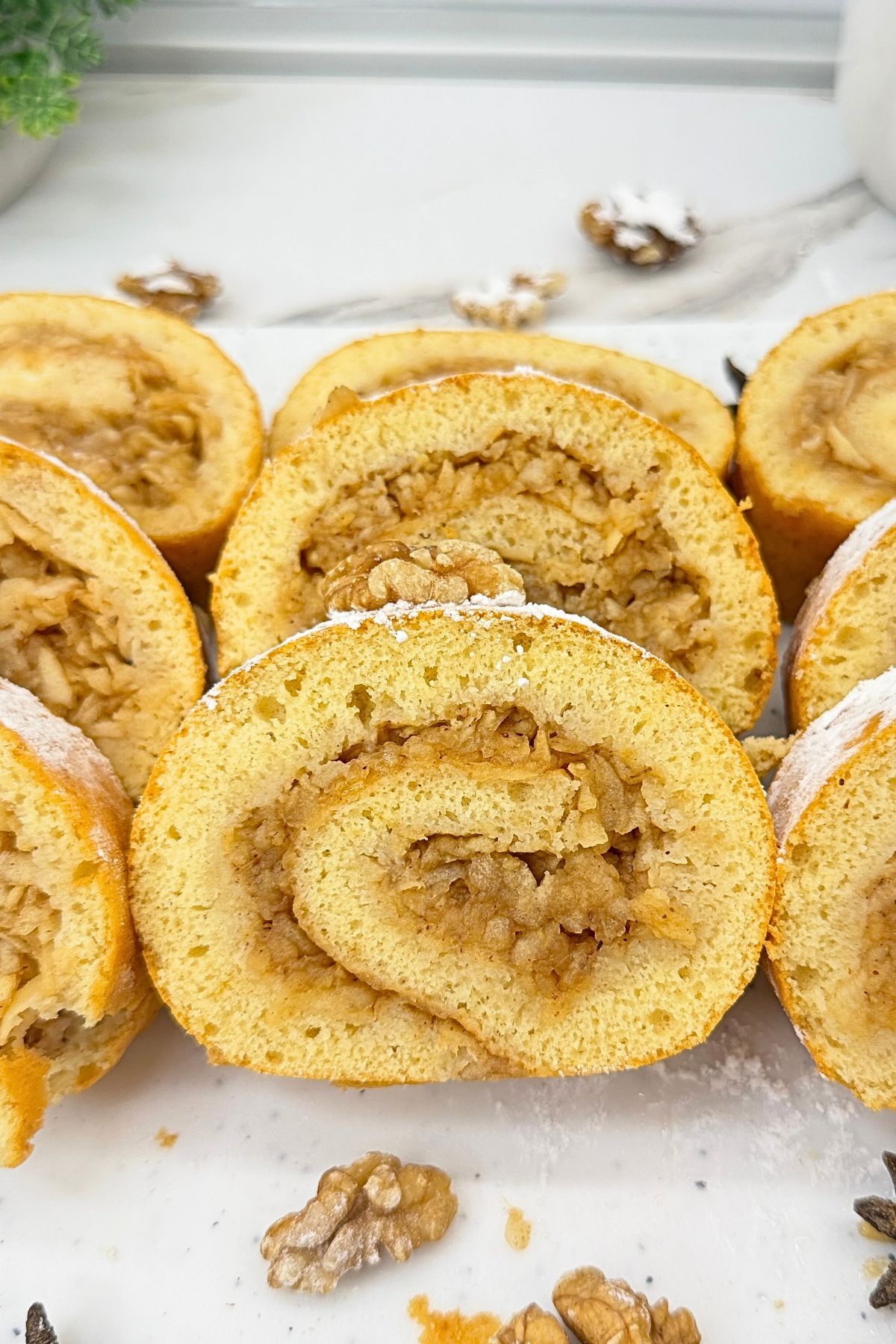 Apple cinnamon cake roll slice with grated apple filling, dusted with powdered sugar and topped with a walnut.