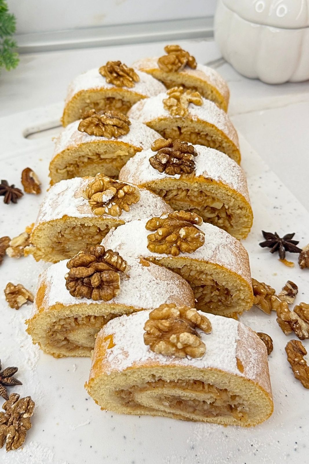 Apple cinnamon cake roll slices dusted with powdered sugar and topped with walnut halves, arranged on a white serving board.