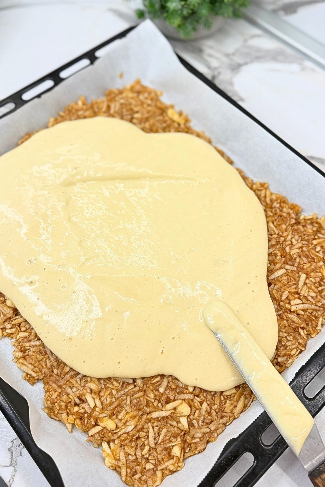 Sponge cake batter being spread over the grated apple filling.