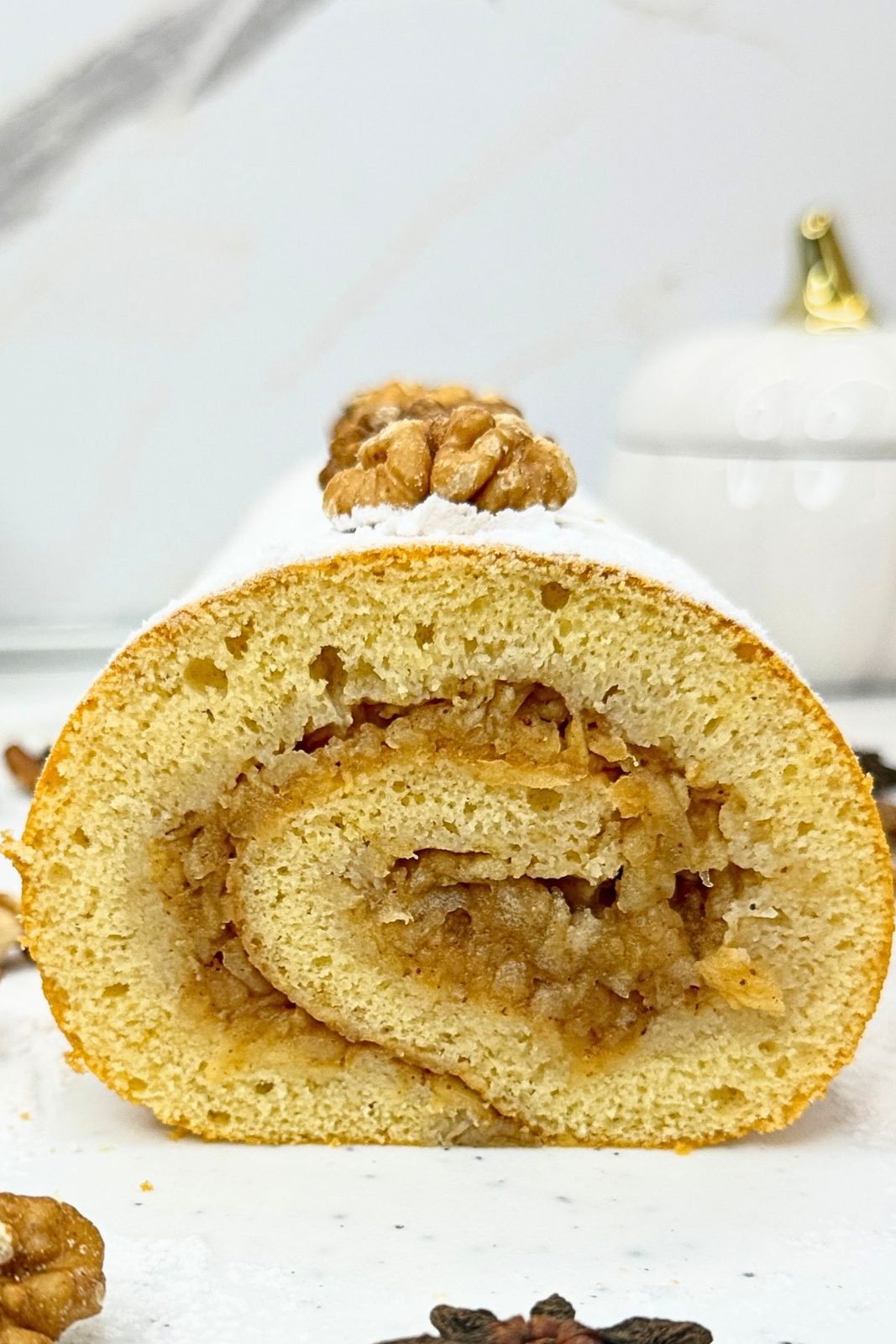 Close-up of an apple cinnamon cake roll showing the apple-filled swirl, topped with powdered sugar and a walnut.