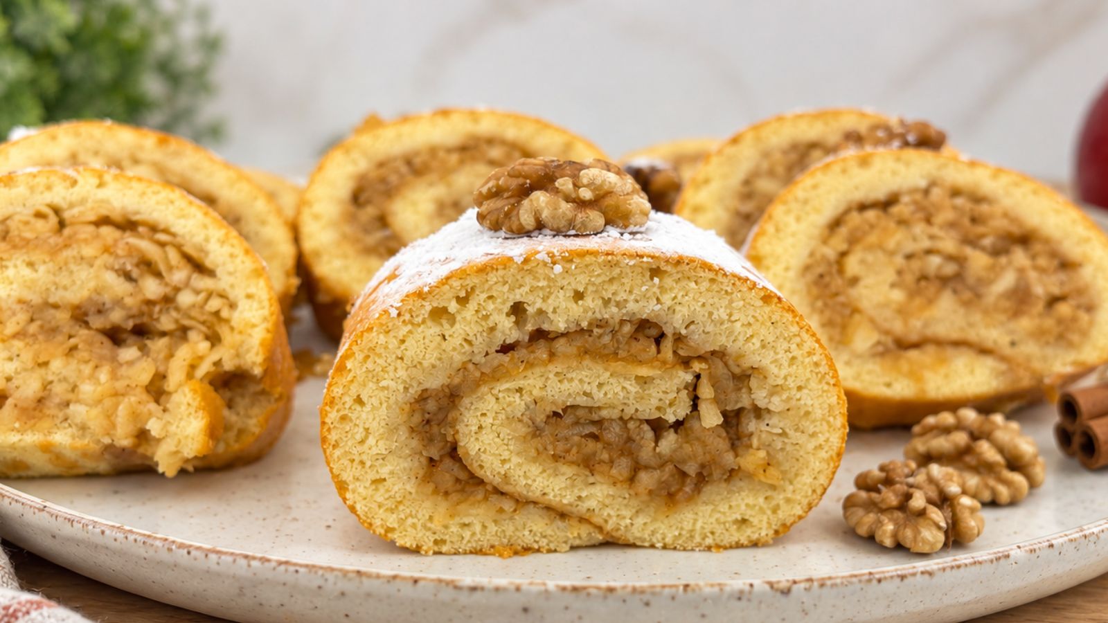 Apple cinnamon cake roll slice with grated apple filling, dusted with powdered sugar and topped with a walnut.