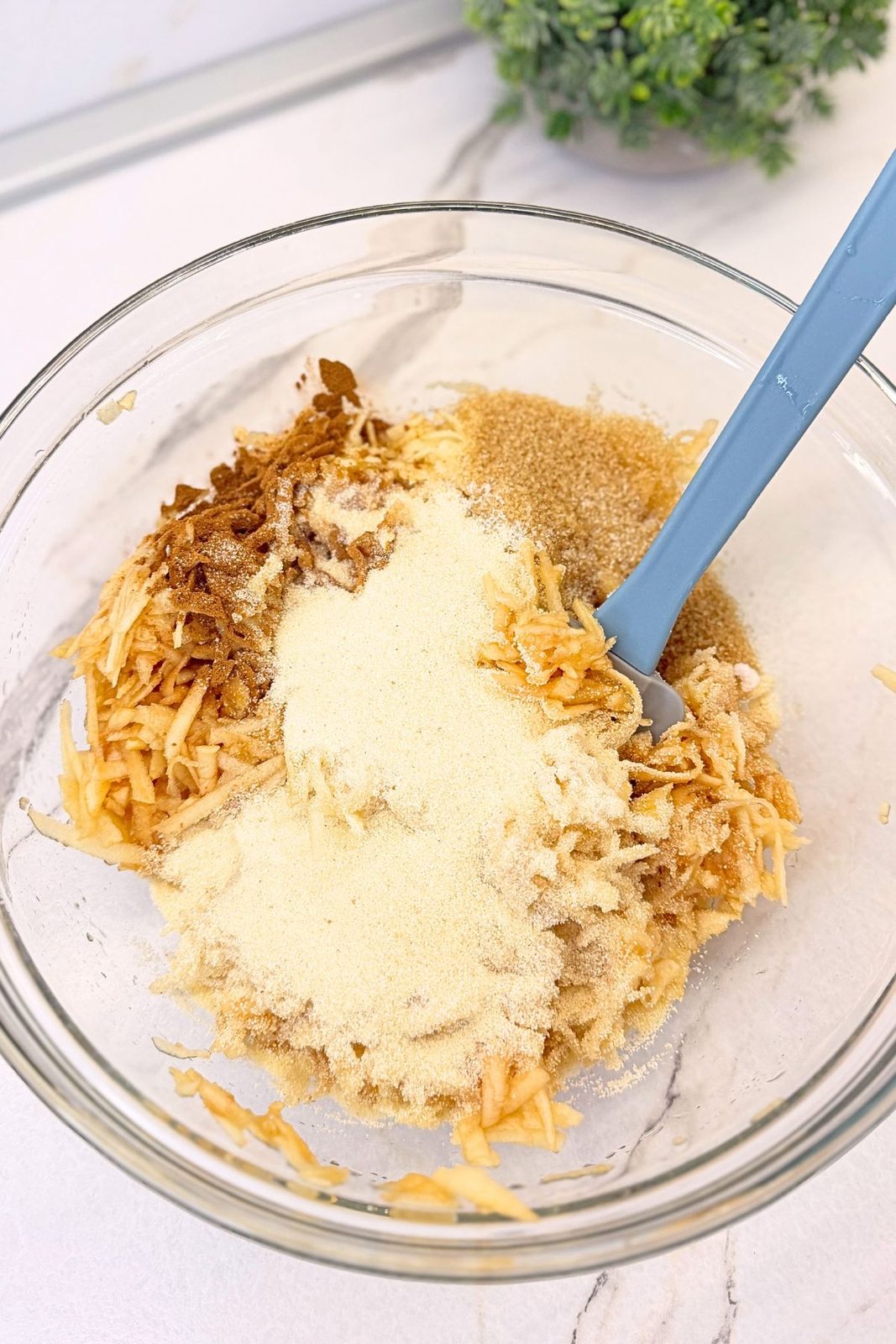 Grated apples in a glass bowl with semolina, brown sugar, and cinnamon for apple phyllo roll filling.