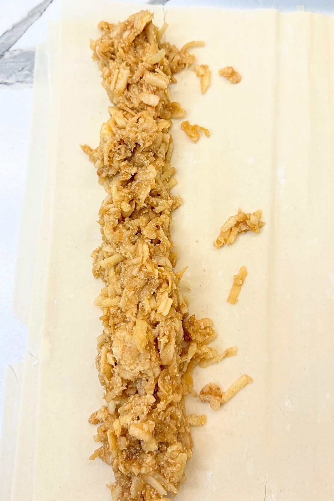 Cinnamon apple filling arranged along one edge of a phyllo sheet before rolling.