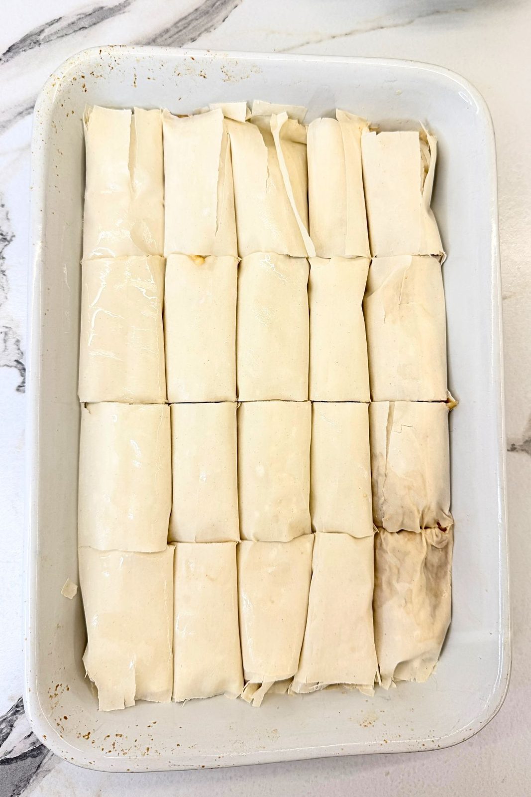 Unbaked apple phyllo rolls cut into portions and arranged in a white baking dish.