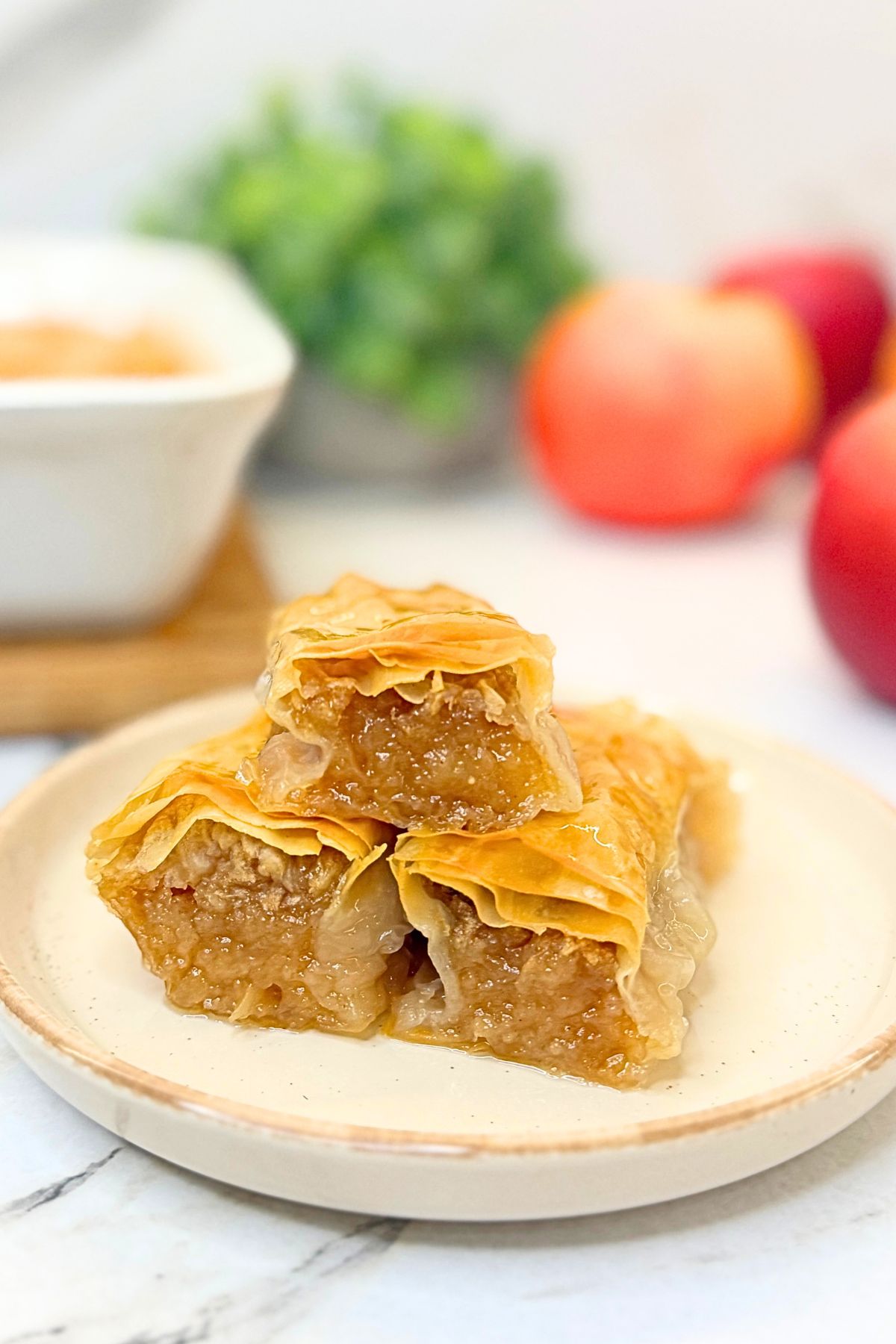 Apple phyllo rolls with vanilla syrup stacked on a ceramic plate, showing golden pastry layers and cinnamon apple filling.