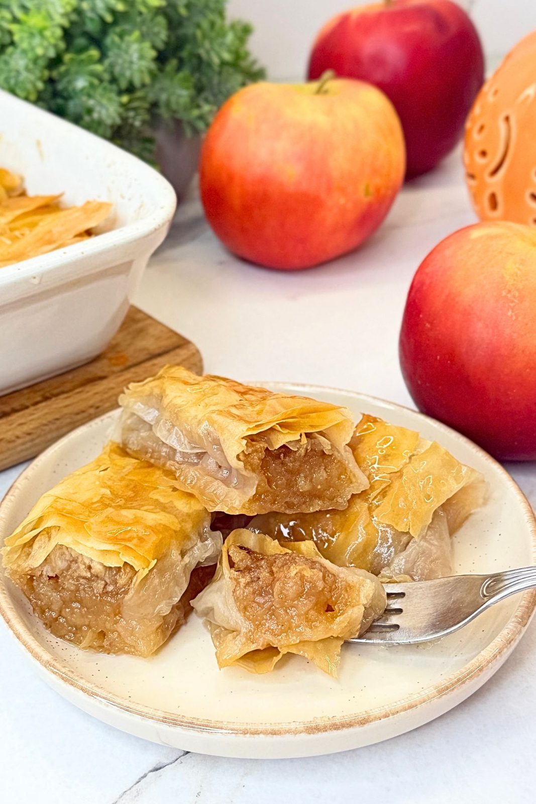 Apple phyllo rolls with vanilla syrup on a plate, with a fork holding a bite of tender cinnamon apple filling and golden pastry.