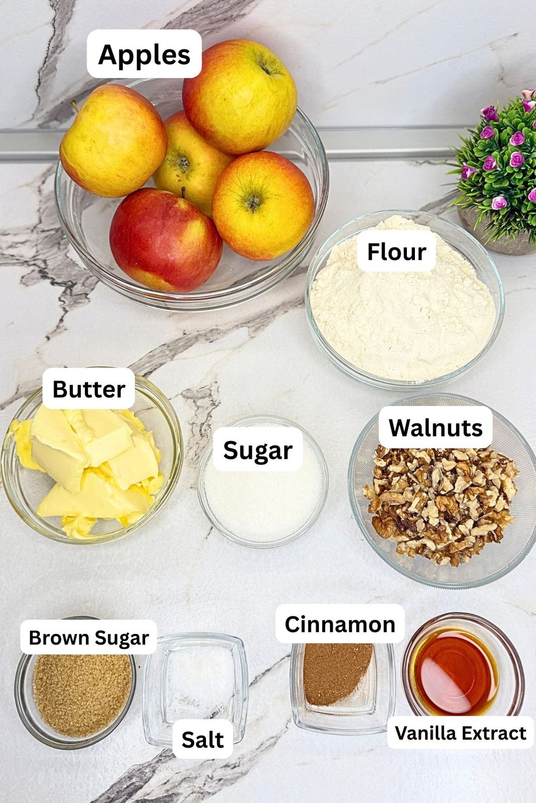 Ingredients for apple pie bars in labeled bowls, including apples, flour, butter, walnuts, granulated sugar, brown sugar, cinnamon, salt, and vanilla extract.