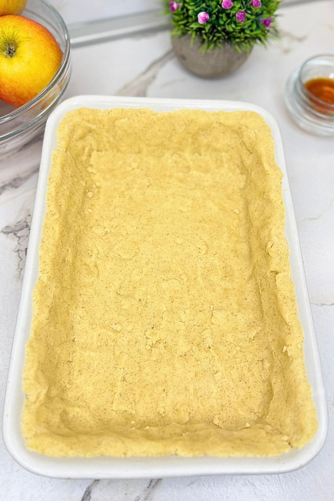 Buttery dough pressed into the bottom and up the sides of a white baking dish for apple pie bars.