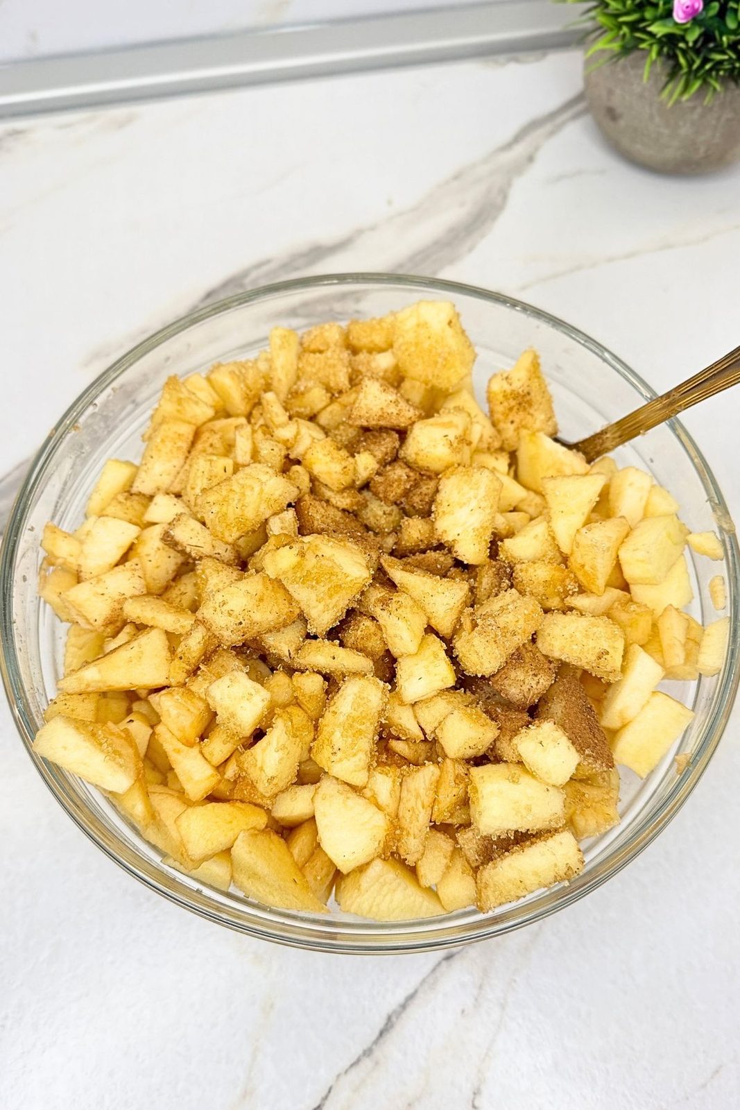 Chopped apples with brown sugar and cinnamon in a glass mixing bowl for apple pie bar filling.