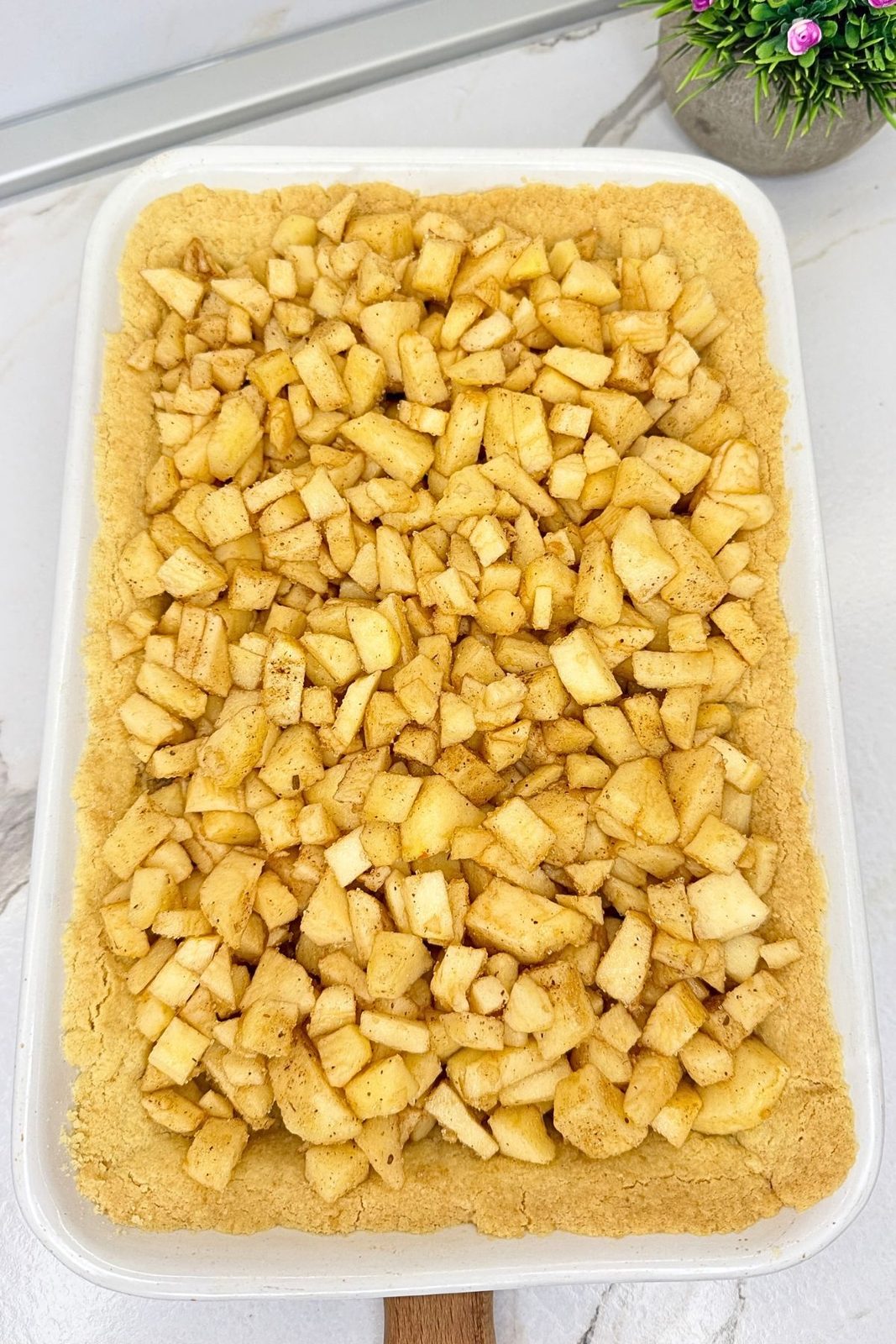 Cinnamon-spiced apple filling spread evenly over the partially baked crust in a white baking dish.