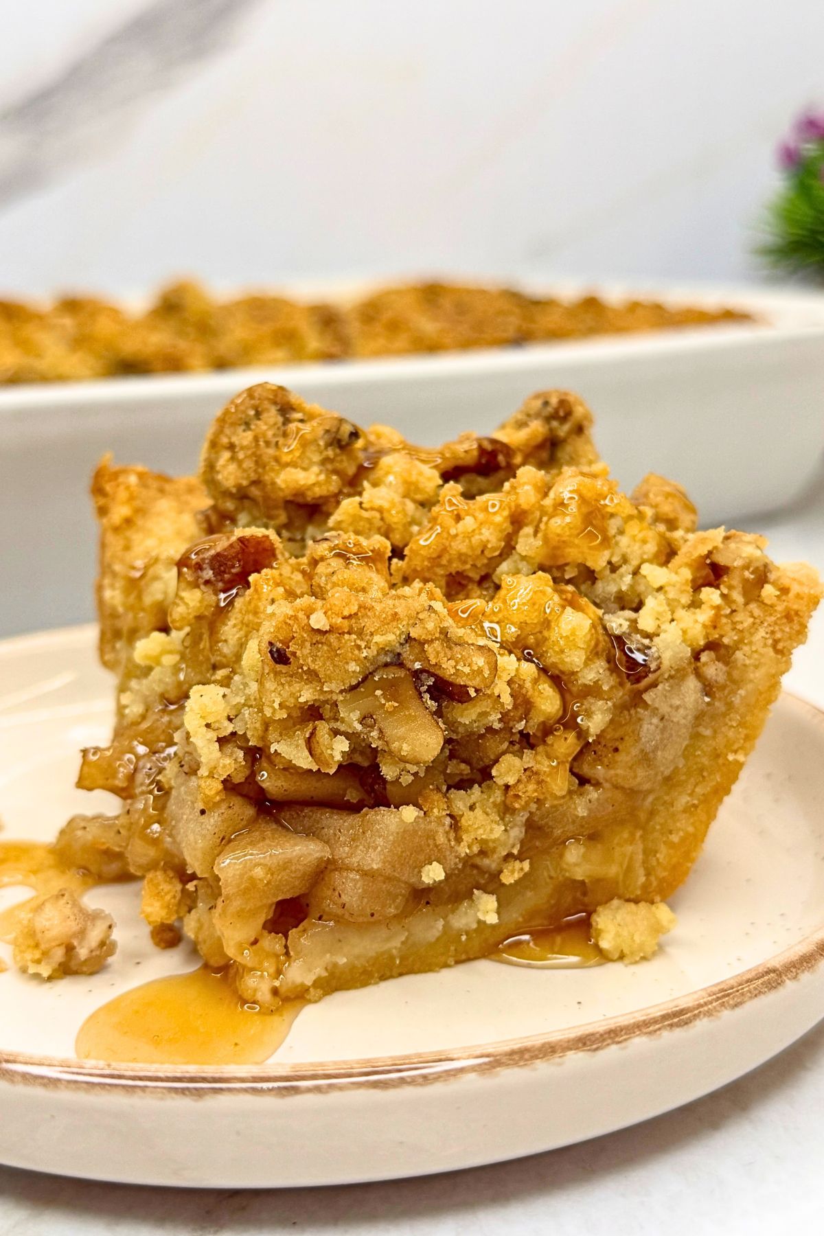 Apple pie bar with a buttery crust, cinnamon apple filling, walnut crumble, and caramel drizzle on a cream-colored plate.