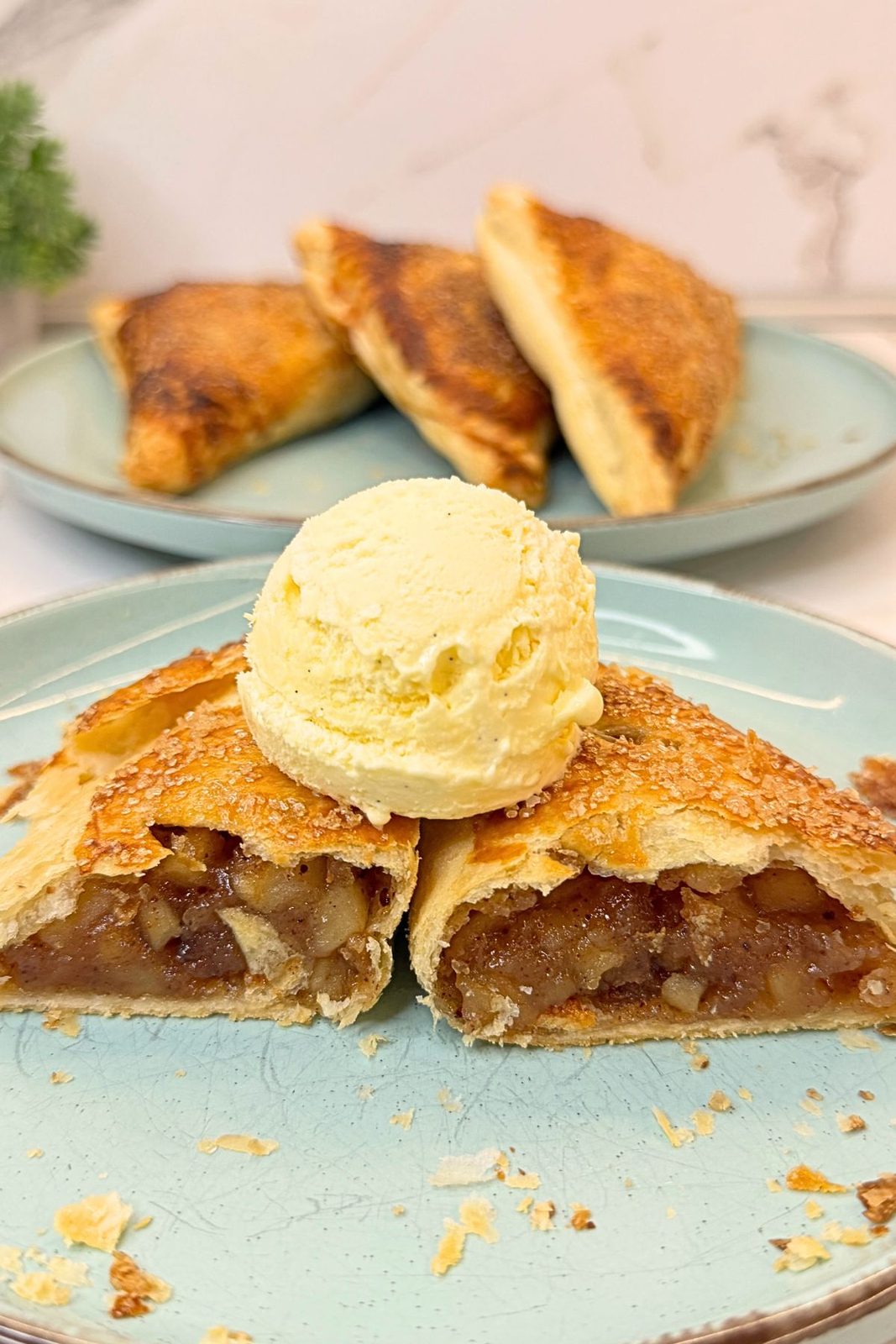 Apple turnovers with flaky puff pastry and cinnamon apple filling, served with a scoop of vanilla ice cream on a blue plate.