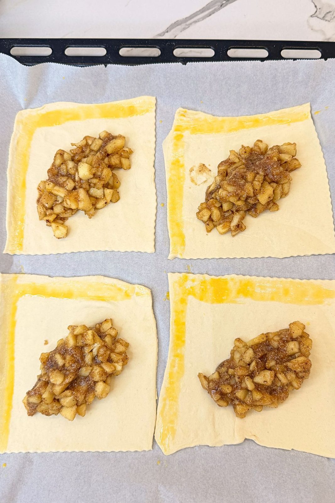 Four puff pastry squares topped with cinnamon apple filling and egg wash brushed along the edges.