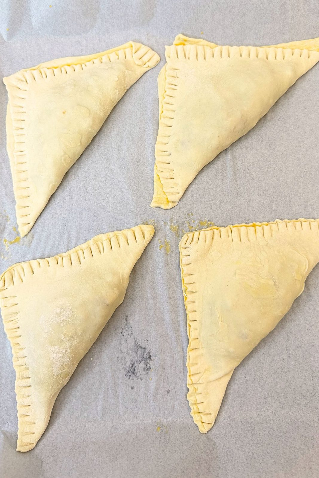 Apple turnovers folded into triangles with fork-crimped edges on parchment paper.