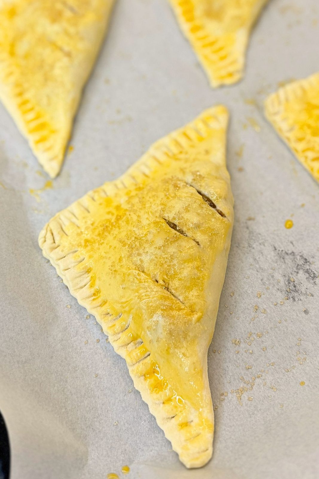 Unbaked apple turnovers brushed with egg wash, sprinkled with sugar, and slit on top to release steam.