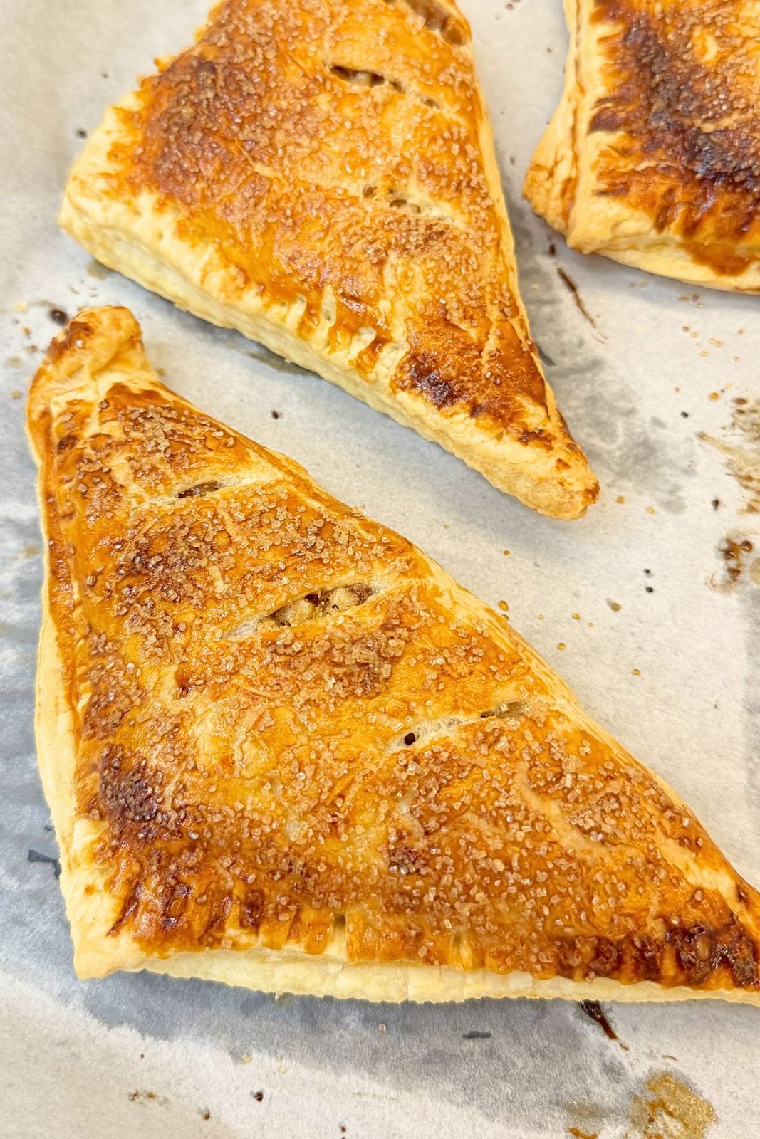 Golden baked apple turnovers with crisp puff pastry and a sugar topping on parchment paper.