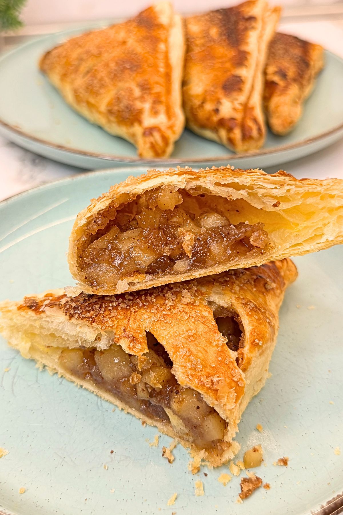 Golden apple turnovers with puff pastry on a blue plate, cut open to reveal the cinnamon apple filling.