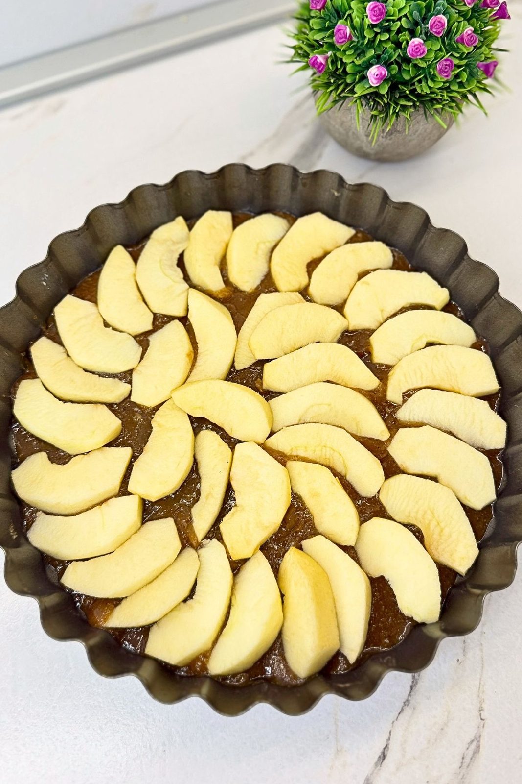 Peeled apple slices arranged over caramel topping in a round baking pan.