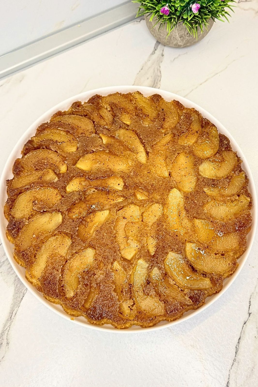 Whole apple upside down cake turned onto a white serving plate, revealing the caramelized apple topping.