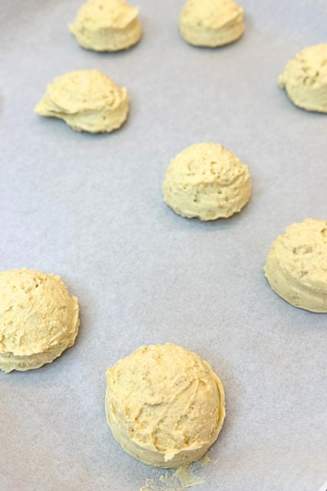 Scoops of cashew cookie dough arranged on a parchment-lined baking sheet